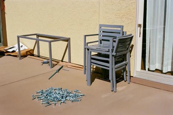 Stacked gray chairs beside a table frame and a pile of screws on a patio.
