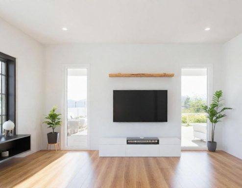 Modern living room with a TV on a white wall, wooden accent, and large windows.