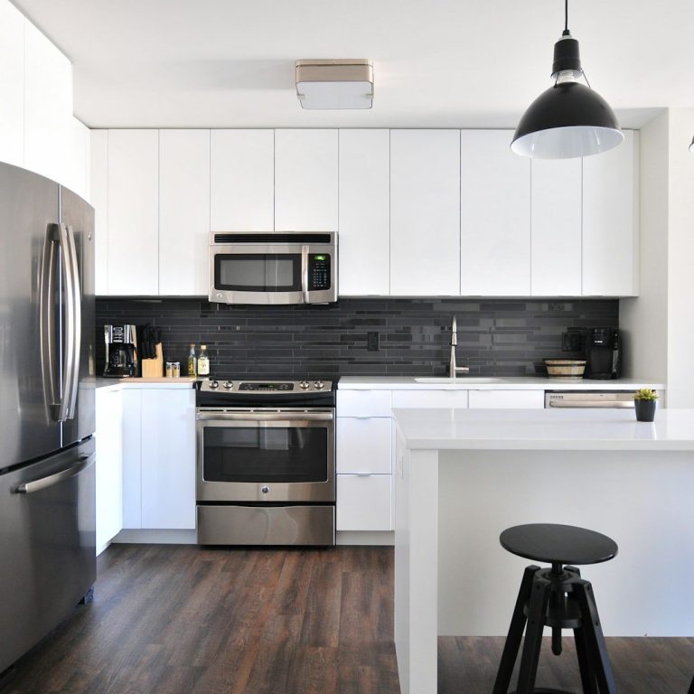 Modern kitchen with stainless steel appliances, white cabinets, and a black tile backsplash.