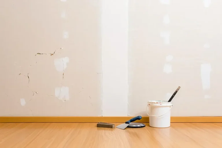 A corner of a room with a paint bucket and tools on the floor near unfinished wall sections.