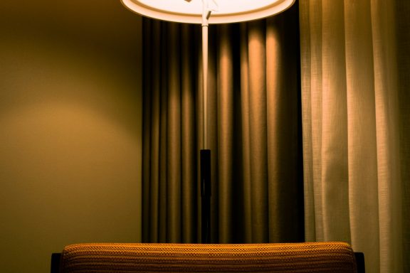 A cozy, dimly lit room featuring a chair and softly draped curtains.